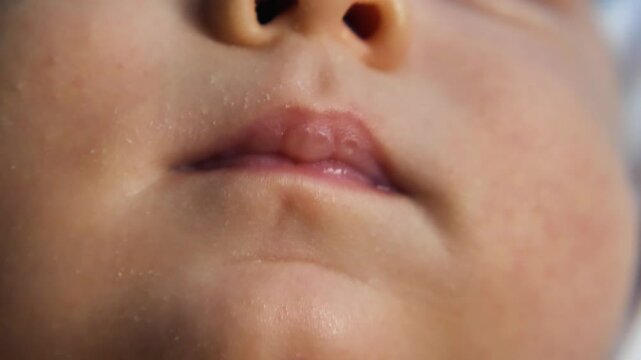 A close-up of a infant's mouth. Chubby pink lips with milk callus slightly ajar the uvula appears. The delicate texture of the baby's skin, including fine facial hair and tiny pores