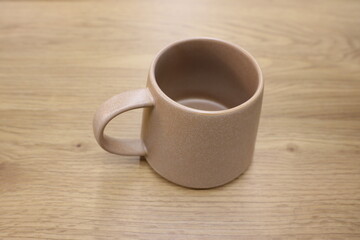 A Simple Yet Elegant Minimalist Beige Ceramic Mug Set Down on a Beautiful Wooden Table