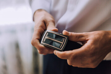 A man is holding a belt with a T on it. The belt is black and gold. The man is wearing a white shirt