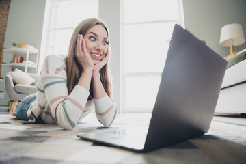 Young woman with a joyful expression discovering something exciting online at home in a cozy living room