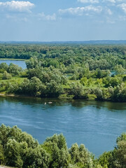 A large and serene body of water, glistening under the sun, is beautifully surrounded by towering trees, all basking in the delightful warmth of a sunny day on a picturesque landscape