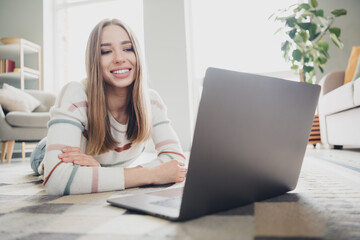 Fototapeta premium Young woman enjoying leisure time at home, smiling while watching a laptop in cozy living room setting, filled with natural daylight.