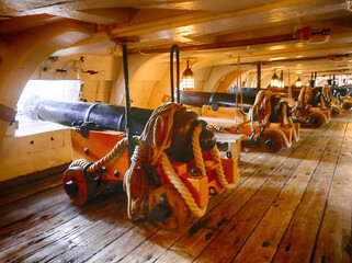 Row of cannons on the gun deck of a warship pointing out to sea