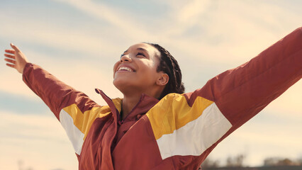 Young Black Woman Joyfully Stretching Her Arms Toward the Sky on a Sunny Day
