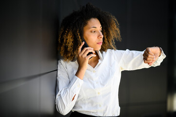 Impatient businesswoman checking time while talking on phone outside office
