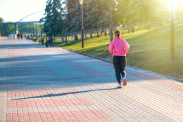 A woman in athletic gear runs along a cobbled embankment on a sunny summer day. Light jogging to stay in shape.