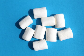 A pile of white marshmallows lies on a blue background.