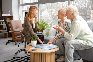 Female travel agent with mature couple and world map planning trip in office