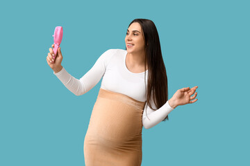 Fototapeta premium Pregnant young woman with small electric fan on blue background