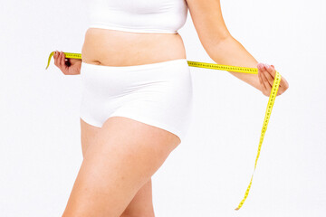 A young plus-size woman measuring her waist against a white background. A concept of weight loss,...