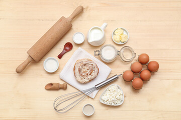 Sweet cinnamon roll and different ingredients on wooden background