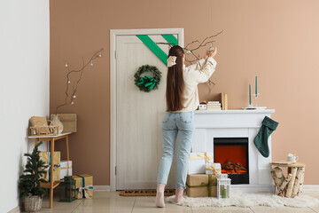 Obraz premium Young woman decorating door for Christmas in hallway