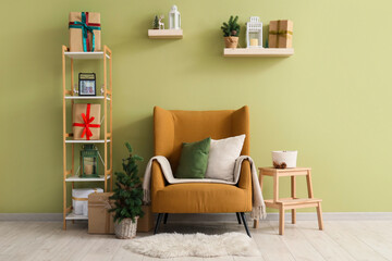 Armchair with cushions, mini fir tree and shelving unit with Christmas gifts near green wall