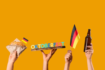Male hands with bottle of cold beer, Germany flags, traditional pretzel and word OKTOBERFEST on orange background. Octoberfest celebration