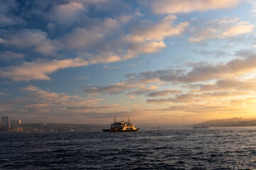 An amazing sunrise over the Bosphorus. Silhouette of a ferry in the vibrant sky, sailing on calm waters. The sky is ablaze with a kaleidoscope of colors, from deep blue to bright orange and yellow.