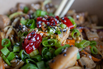Close-up of stir-fried noodles with vegetables, sesame seeds, and spicy sauce, garnished with green onions