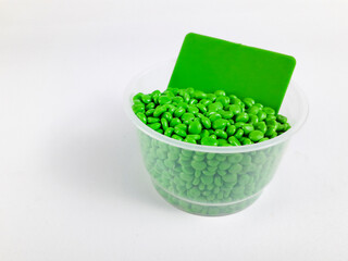 Green masterbatch granules in a cup with color chip as a sample of the resulting color, isolated on...