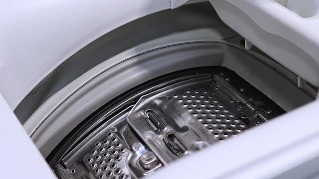 Woman closing drum in top-loading washing machine, preparing for wash cycle