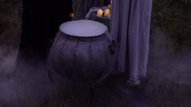 Close-up magic cauldron with mysterious potion and thick steam smoke from a big vintage black pot with women witches and burning candles 4K