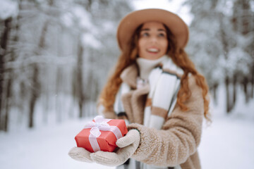 Portrait of happy woman holding festive red gift box in her hands background in winter forest. Winter holidays.