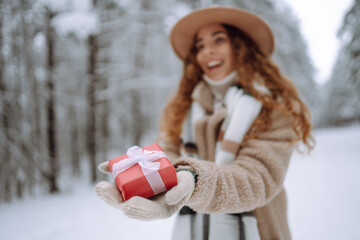 Portrait of happy woman holding festive red gift box in her hands background in winter forest. Winter holidays.