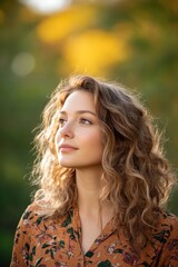 Naklejka premium Thoughtful young woman with curly hair and floral blouse in nature