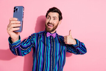 Photo of attractive bearded elegant man wear trendy striped clothes make video selfie thumb up isolated on pink color background