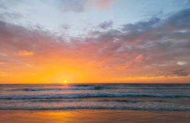 Beautiful sunset at sea. Waves, illuminated by the rays of the setting sun, roll onto the shore. In the sky, clouds in the rays of the sunset. Travel and Tourism Concept