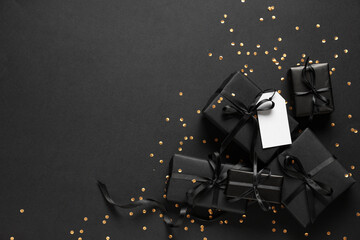 Gift boxes with blank paper tag, confetti and ribbons on black background. Black Friday sale