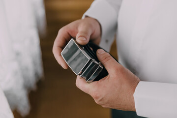 A man is holding a small black box with a silver band. The box is rectangular and has a silver band around it