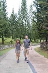 Fototapeta premium A Chinese-Malaysian couple in their 30s walk together in a green park with abundant water in Kuala Lumpur, Malaysia, on a sunny day in June 2024.