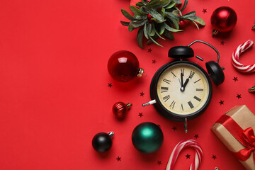 Composition with alarm clock, decorations, candy cane, mistletoe and confetti on red background. Christmas countdown concept. Top view