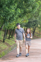 A Chinese-Malaysian couple in their 30s walk together in a green park with abundant water in Kuala Lumpur, Malaysia, on a sunny day in June 2024.