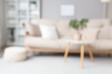 Blurred view of light living room with beige sofa, table and shelf unit