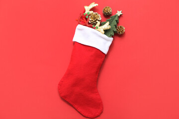 Obraz premium Christmas sock with reindeer horns, cones and fir tree on red background. Top view