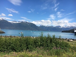 Stunning panoramic view of a serene lake surrounded by snow-capped mountains under a blue sky with wispy clouds. 