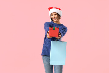 Beautiful young happy woman in Santa hat with shopping bag and gift box on pink background. Christmas celebration
