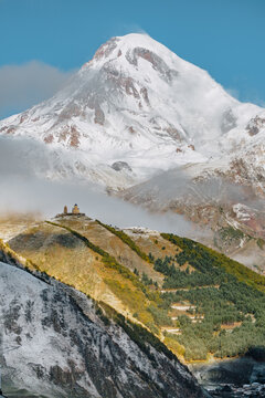 Gergeti Trinity Church perched on a hill with the snow-covered Mount Kazbek towering in the background, under a vibrant blue sky in Georgia.