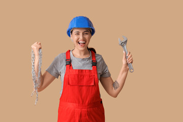 Young female construction worker with wrench and chain on beige background. Woman in male...