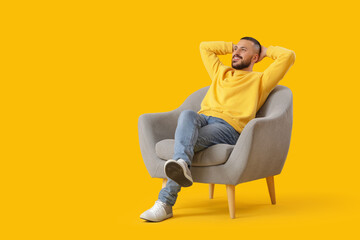 Young man resting in armchair on yellow background. Day off concept