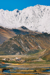 Obraz premium Alpine landscape with the village of Ketrisi, winding rivers, snowy peaks, and a serene trail under a clear blue sky in the Truso Gorge, near Kazbegi, Georgia