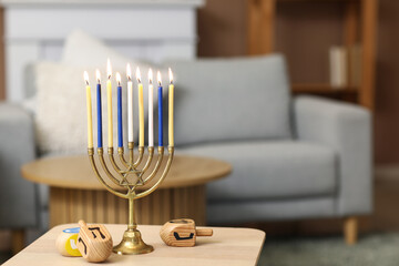 Menorah with burning candles and dreidels on table at home, closeup. Hanukkah celebration