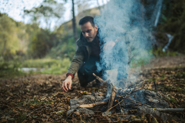 Adult man hiker kneel and make a fire with wood ready for camping
