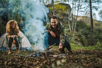 Adult man hiker kneel and make a fire with wood ready for camping