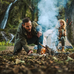 Adult man hiker kneel and make a fire with wood ready for camping
