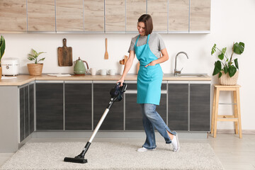 Beautiful young woman cleaning floor with modern vacuum cleaner in kitchen