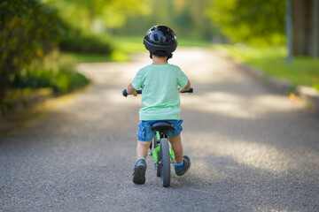 Little boy with helmet running and riding on first bike without pedals on sidewalk at city park in...