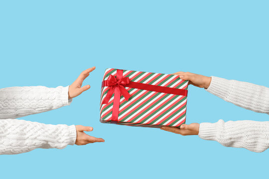 Female hands passing Christmas gift on blue background