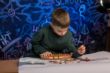 A child in a green sweatshirt building a model ship, immersed in a creative project, symbolizing...