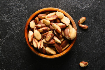 Wooden bowl with tasty Brazil nuts on black background
